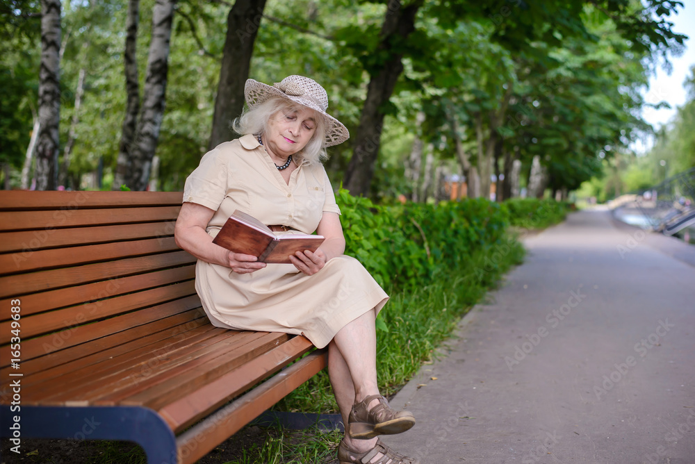 Fototapeta premium An elderly woman reads a book in the park