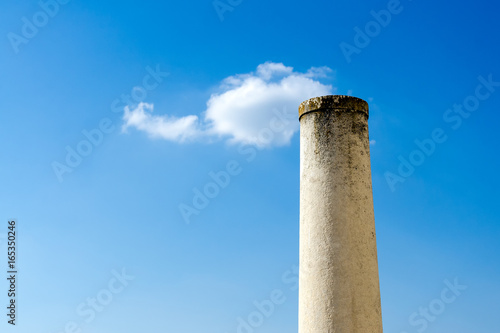 Stone column with small puffy cloud on top against blue sky