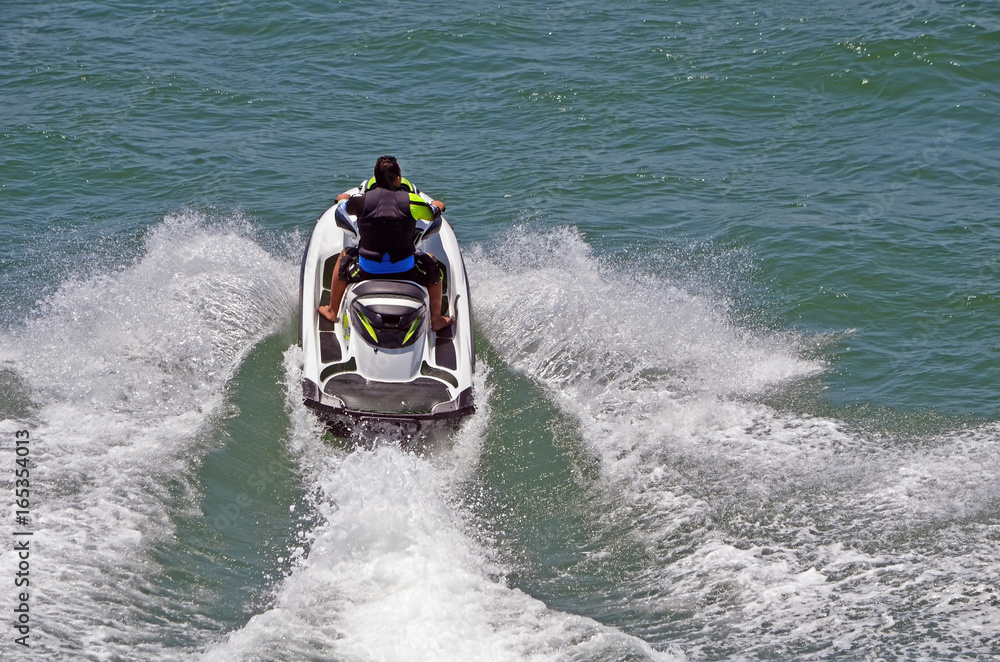 Angled overhead view of a young man riding waves on a speeding jet ski.