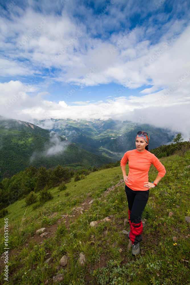a woman tourist stands at the top of a hill  on a background of mountains