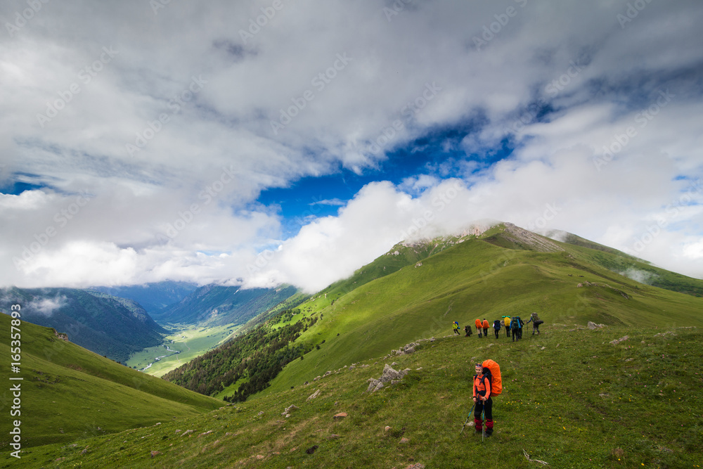 a woman tourist stands at the top of a hill with a backpack on a background of mountains