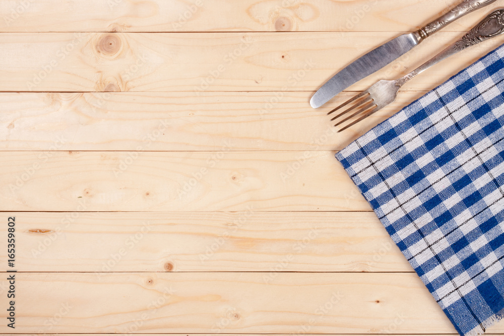 blue checkered tablecloth with knife and fork on a light wooden table with copy space for your text. Top view