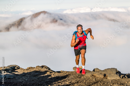 Fotografie, Obraz Runner trail running fitness man on endurance run - motivation and concentration on race in sky and clouds background on nature landscape