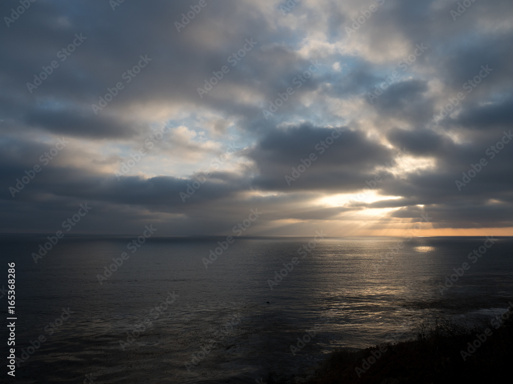 Beams of sunlight show through a cloudy sky onto the ocean