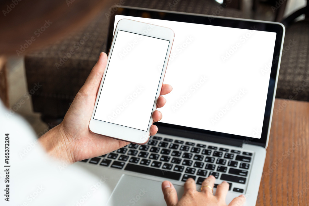 Hand holding the technology smart mobile phone shown white background for product mockup over the photo blurred of laptop with white background, business and technology concept Hand holding the technology smart mobile phone shown white background for product mockup over the photo blurred of laptop with white background, business and technology concept
