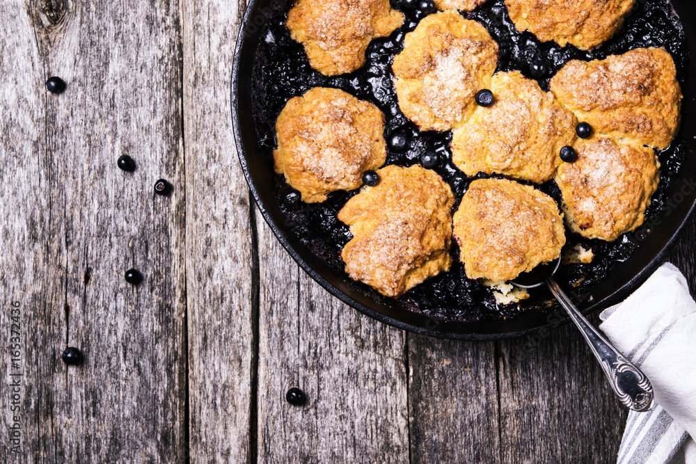 Homemade Blueberry cobbler in a cast iron skillet pan on a rustic wooden table. Organic natural food. Healthy breakfast. Top view. Selective focus Homemade Blueberry cobbler in a cast iron skillet pan on a rustic wooden table. Organic natural food. Healthy breakfast. Top view. Selective focus