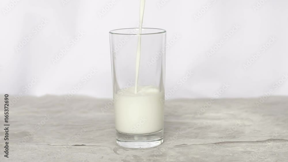 Milk pouring into a glass on white background, slow motion. Milk pouring into a glass on white background, slow motion.