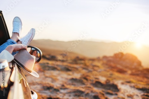 Cuadro en lienzo Happy young woman rests and pushes her sneakers out of the convertible to enjoy