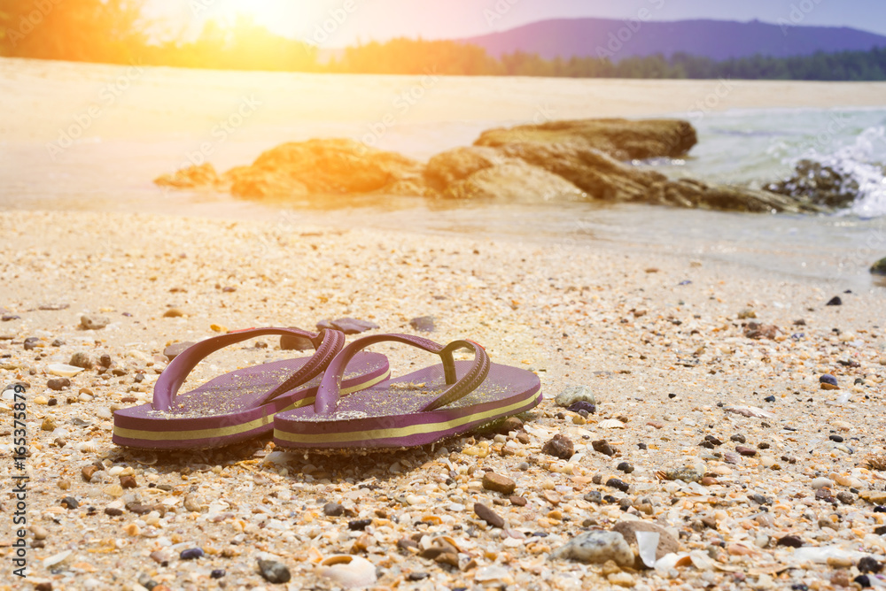 Violet flip flops against the sandy beach of the brown beach on weekends.