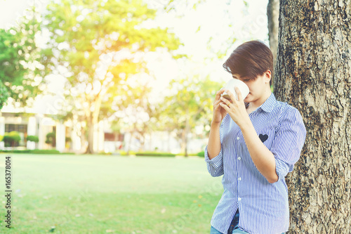 Beautiful short hair woman standing in the green yard and drinking a favorite beverage in white cup for resting between her outdoor working business in the park.