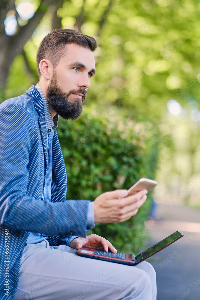 Fototapeta premium Stylish bearded male in a blue jacket using smartphone.