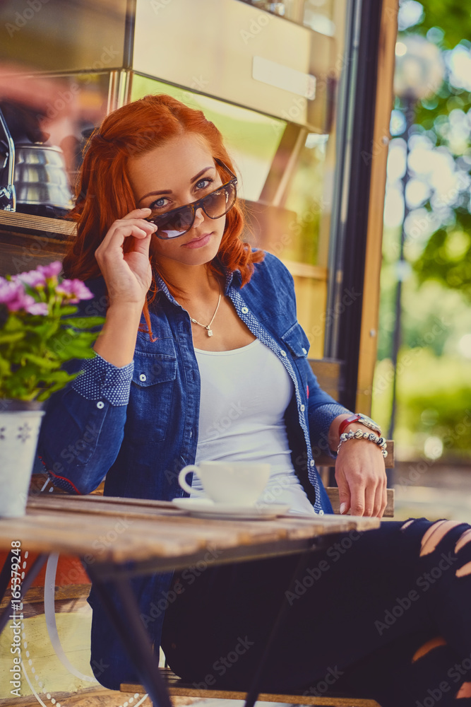 Redhead female drinks coffee in a cafe.