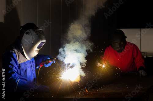 Welder with personal protective equipment and protective mask welding steel pipe in factory.