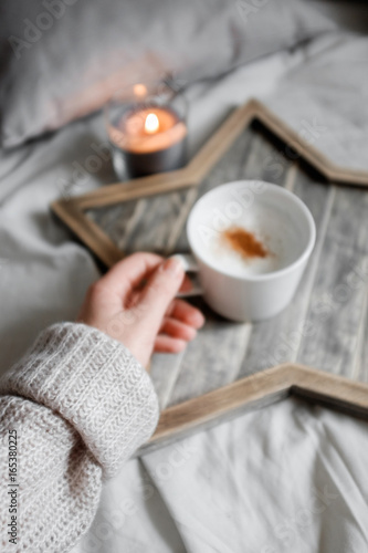 A girl in a sweater holds a cup of coffee on a designer wooden tray