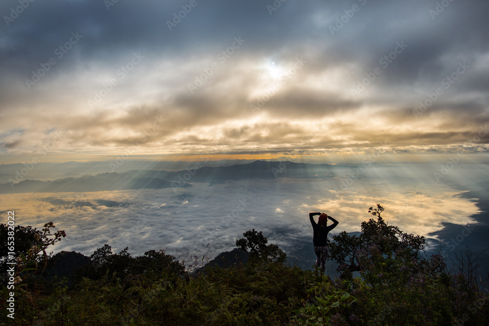 cheering girl put arms on her head at mountain peak with crepuscular rays