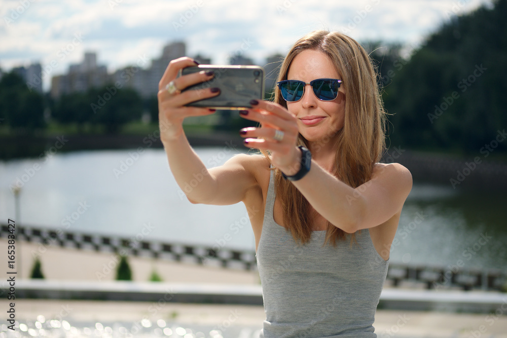 Attractive tourist girl making selfie with river bank on background in city park