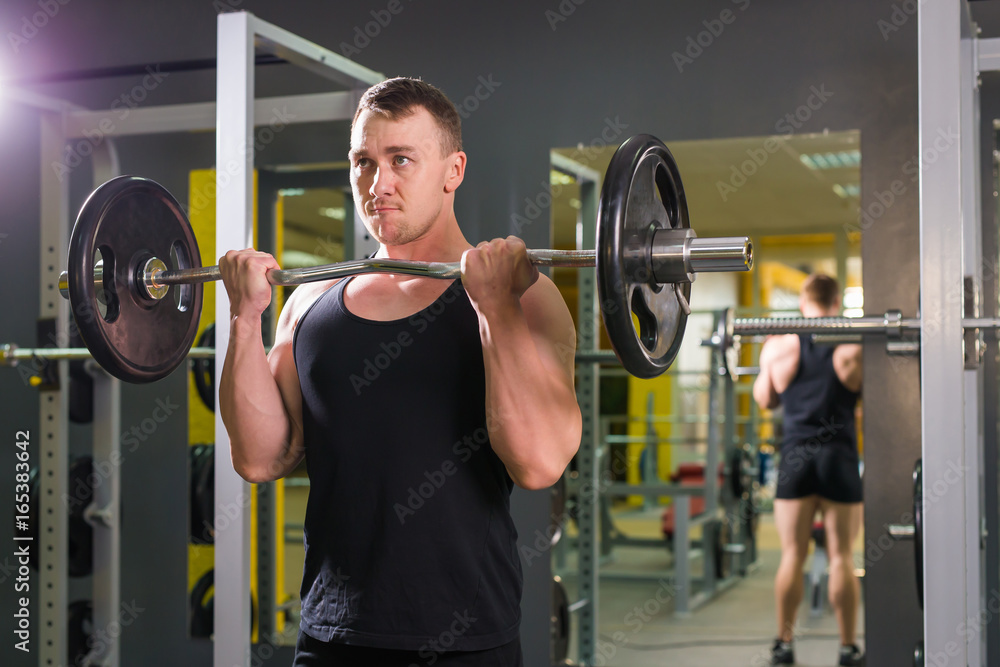 Muscular man with pulling up barbell in fitness training class indoors