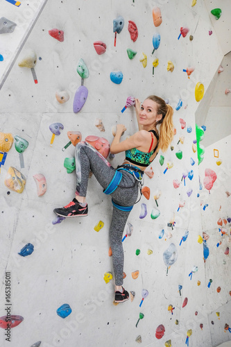 Woman climbing on climbing wall. Teenage rock climber in sportswear and equipment.