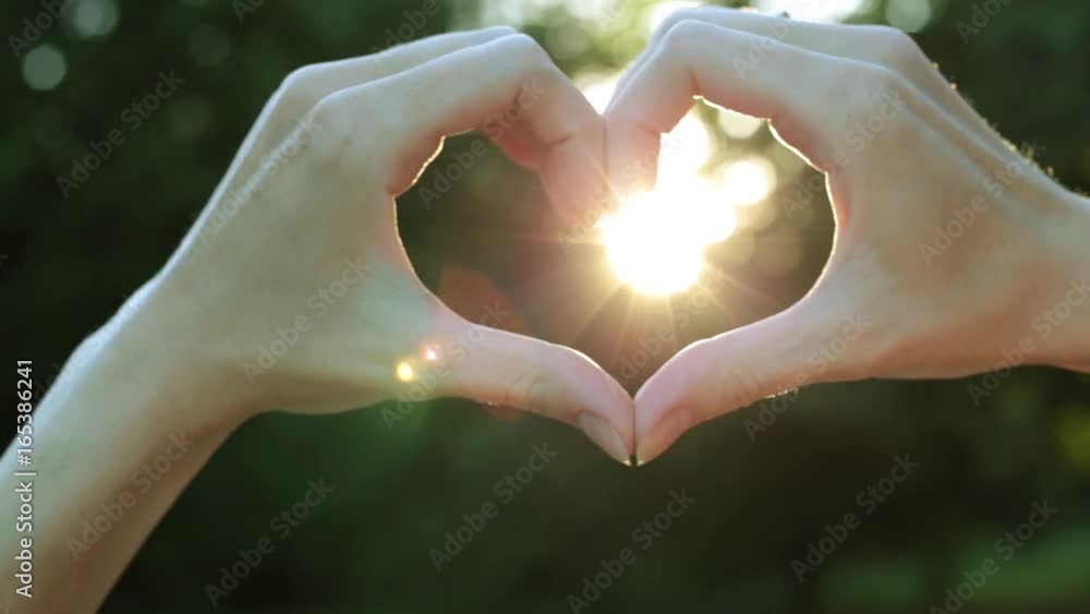 Female hands in the shape of heart against the background of the sun. Female fingers in the shape of heart. Female hands in the shape of heart against the background of the sun. Female fingers in the shape of heart.