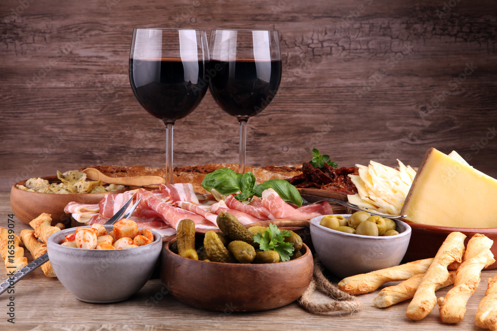 Italian antipasti wine snacks set. Cheese variety, Mediterranean olives, pickles, Prosciutto di Parma, tomatoes, artichokes and wine in glasses Italian antipasti wine snacks set. Cheese variety, Mediterranean olives, pickles, Prosciutto di Parma, tomatoes, artichokes and wine in glasses