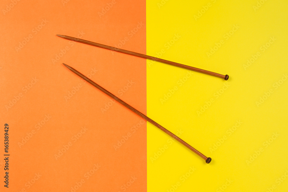 Pair of wooden knitting needles on yellow and orange background