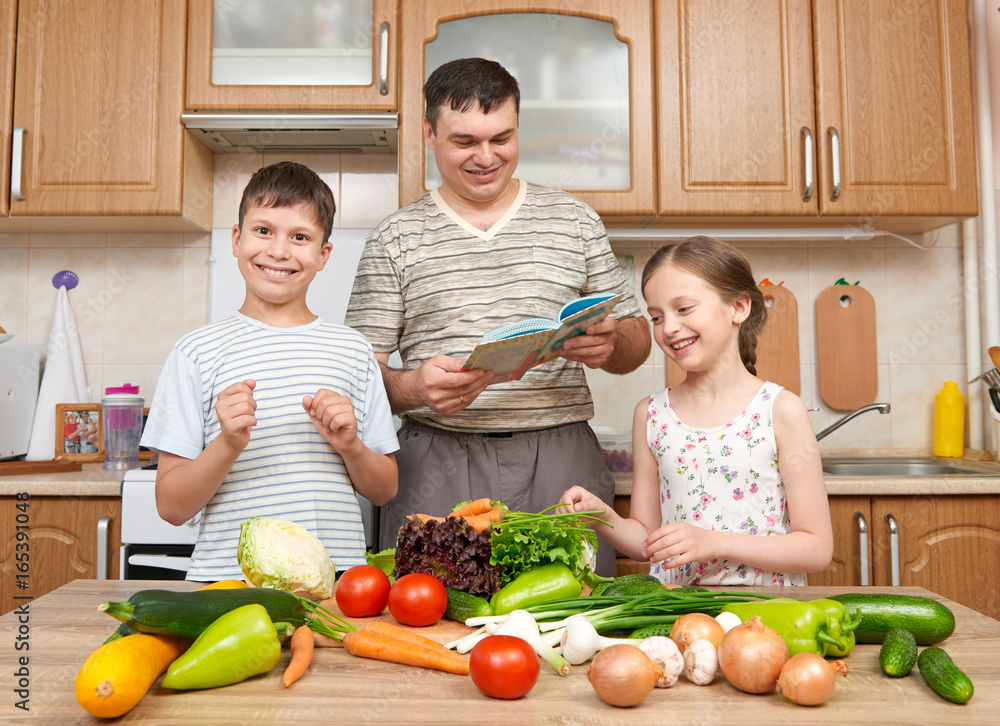 Father and two children reading cooking book and choice dishes. Happy family, girl and boy having fun with fruits and vegetables in home kitchen interior. Healthy food concept. Father and two children reading cooking book and choice dishes. Happy family, girl and boy having fun with fruits and vegetables in home kitchen interior. Healthy food concept.