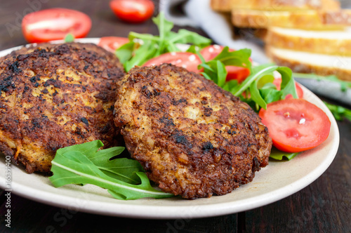 Juicy cutlets on a plate with a salad of tomatoes and arugula on a dark wooden background.