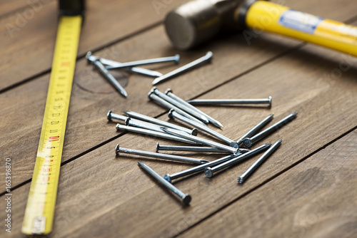 Stacked nails next to a hammer and tape measure on brown wooden table. Construction tools