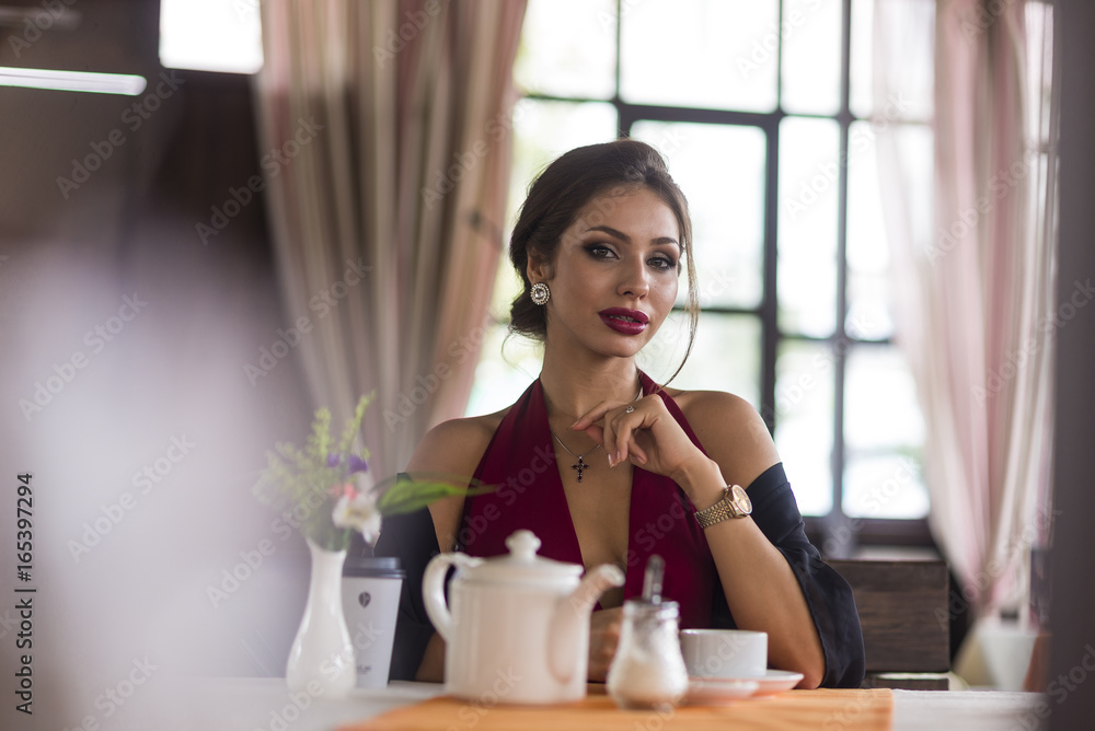Young business woman grinks coffee at a cafe. Smiling and flirts. Looks at camera Young business woman grinks coffee at a cafe. Smiling and flirts. Looks at camera