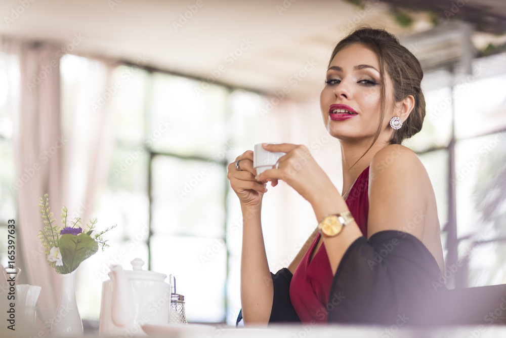 Young business woman grinks coffee at a cafe. Smiling and flirts. Looks at camera Young business woman grinks coffee at a cafe. Smiling and flirts. Looks at camera