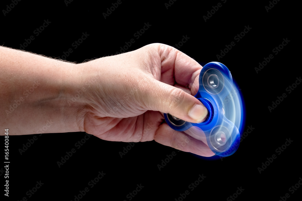 Spinning fidget spinner toy in human left hand isolated on black background. Super popular device.