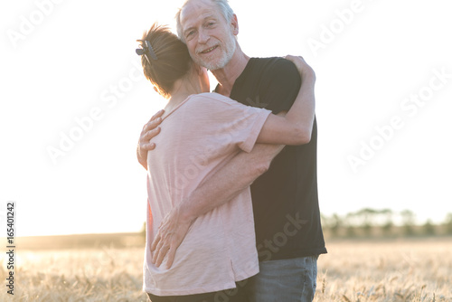 Senior couple embracing each other in a wheat field, sunlight effect