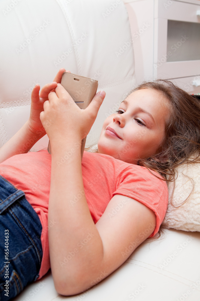 girl playing in the mobile phone lying on a sofa girl playing in the mobile phone lying on a sofa