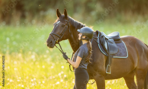 Young woman rider with her horse in evening sunset light
