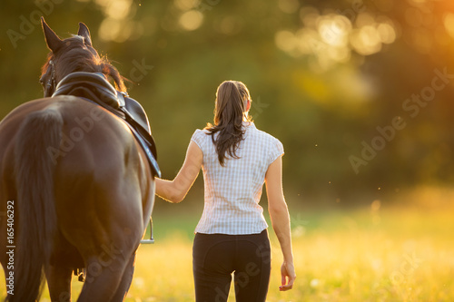 Backview of young woman walking with her horse in evening sunset light