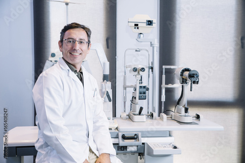 Portrait of handsome eye doctor sitting with ophthalmologic device in the cabinet