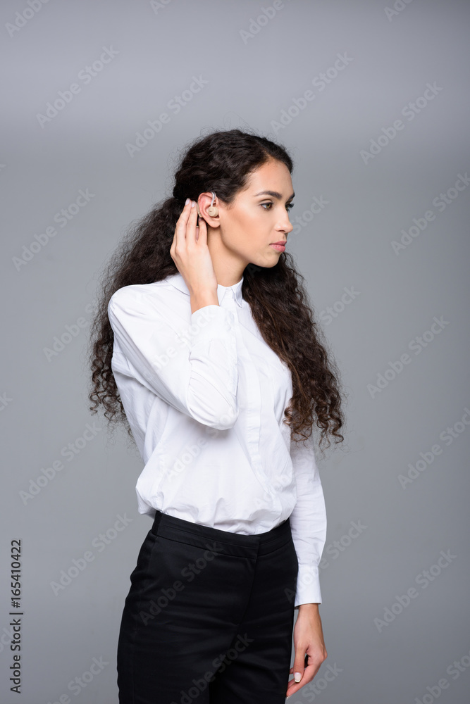 attractive brunette woman with hearing aid, isolated on grey attractive brunette woman with hearing aid, isolated on grey