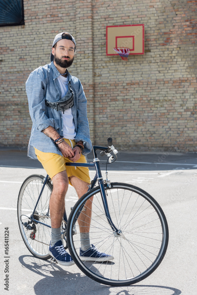 hipster man sitting on bicycle and looking at camera on street