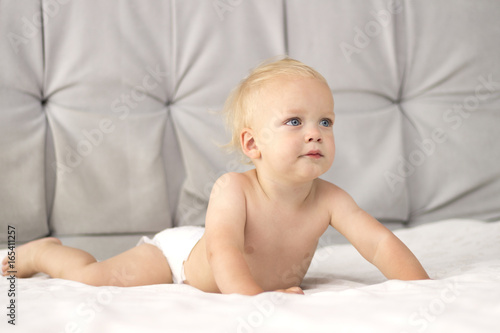 CUte toddler in a diaper lying on the white blanket against the grey background. Copy space