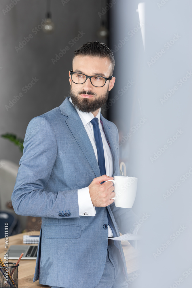 side view of pensive businessman with coffee cup in hand looking away in office side view of pensive businessman with coffee cup in hand looking away in office