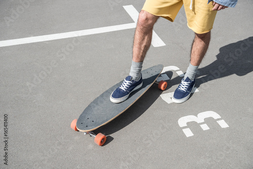 cropped shot of man in shorts standing on longboard on street