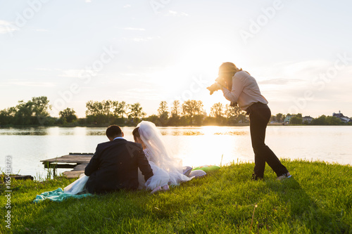 Wedding photographer photographs brides sitting on the lake. Sunset, the sun shines in the camera.