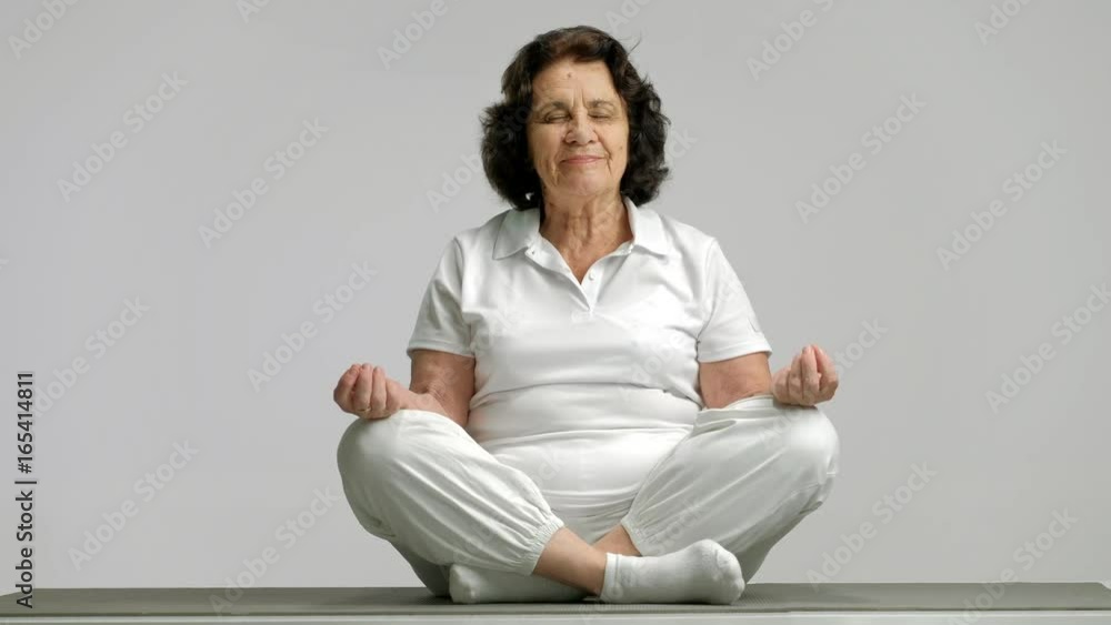 Elderly woman meditating on an exercise mat Elderly woman meditating on an exercise mat
