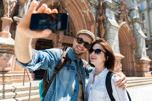 Cheerful youthful couple using gadget when sightseeing