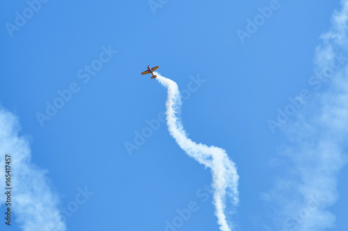 View on sport plane vapour trail in shape of spiral. White vapour trail track on blue sky background. Sport plane Aerobatic maneuver stunt. Spinning plane vapor trail in the sky. photo