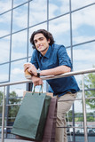 smiling young man holding shopping bags and drinking coffee from paper cup