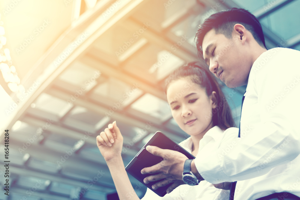 Two asian business standing under office company building with looking information financial on tablet screen and searching data result.