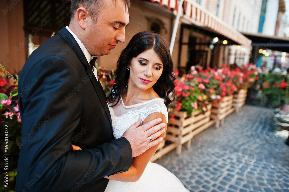 Amazing young attractive newly married couple walking and posing in the downtown with beautiful architecture and flowers on the background on their wedding day. Amazing young attractive newly married couple walking and posing in the downtown with beautiful architecture and flowers on the background on their wedding day.