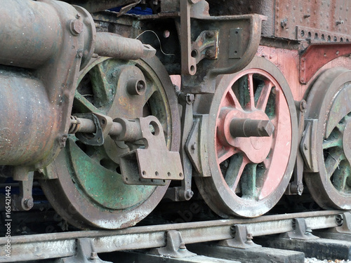 Old wrecked steam locomotive on tracks with rust fading green and red paint and missing parts