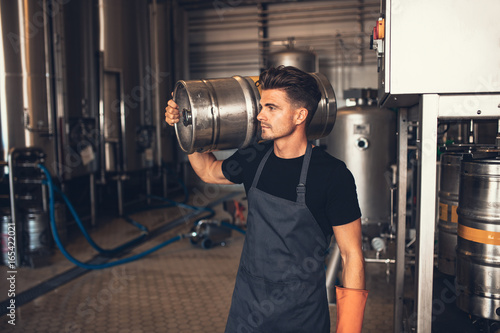 Billede på lærred Young male brewer carrying keg at brewery